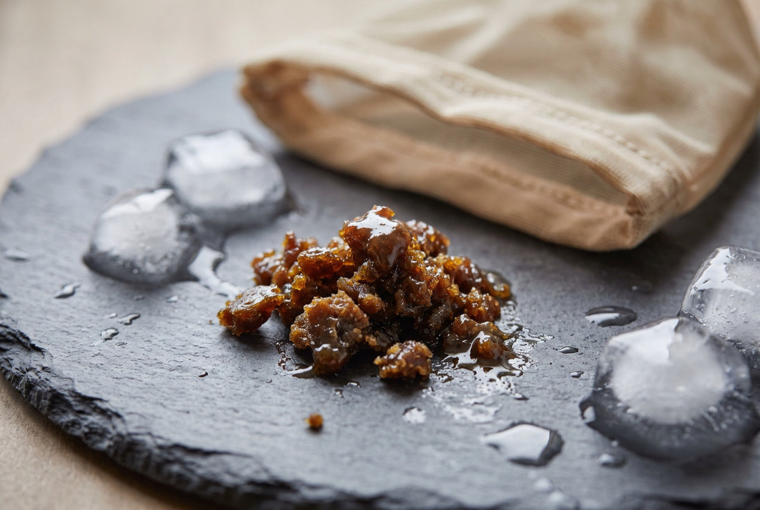 Bubble hash CBD, résine sombre et grasse, posée sur une ardoise à côté de glaçons et d'un sac de filtration
