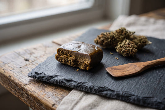 Bloc de résine de hash CBD artisanale sur une ardoise, avec des fleurs de chanvre séchées